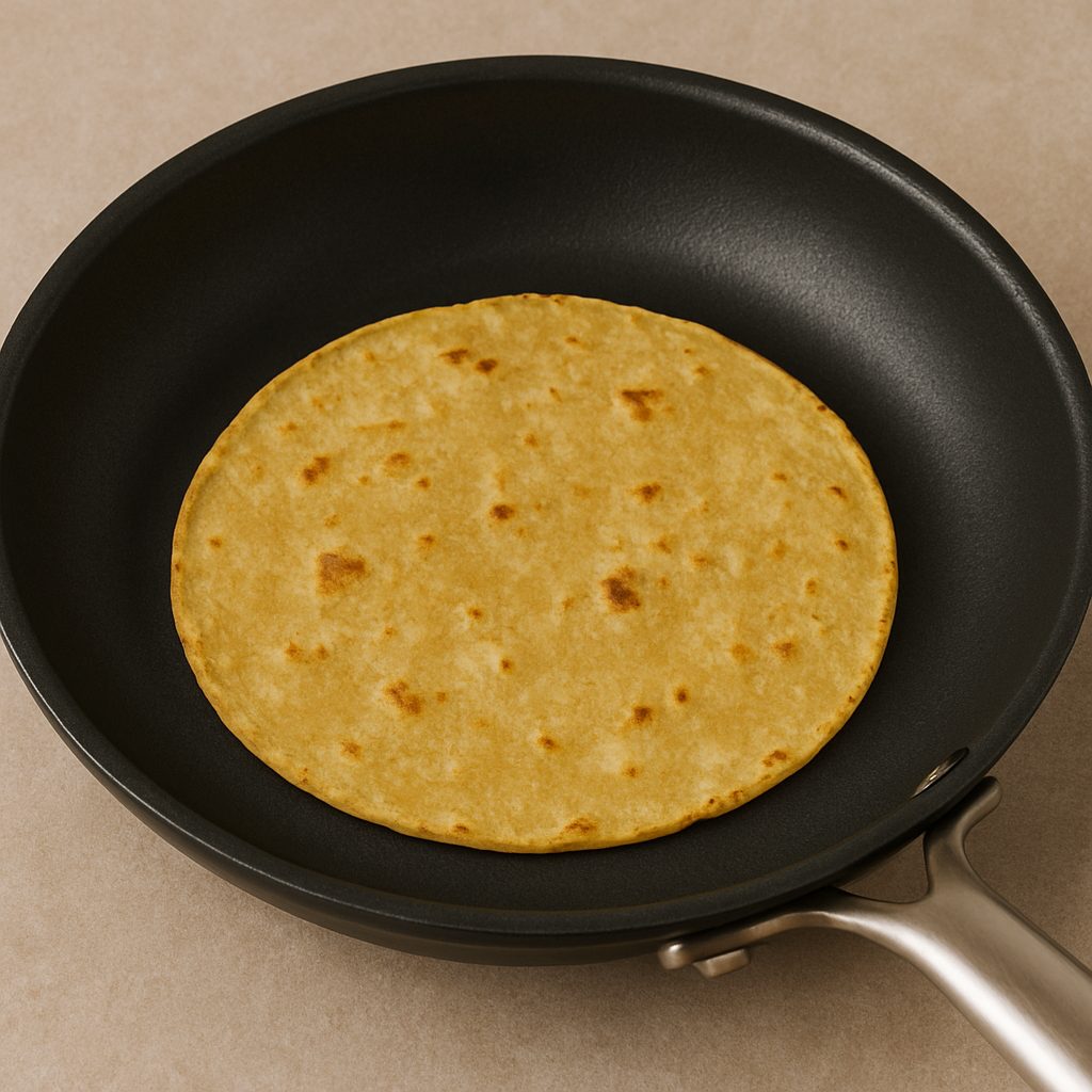 Tortilla de maíz calentándose en una sartén hasta estar suave y ligeramente dorada.