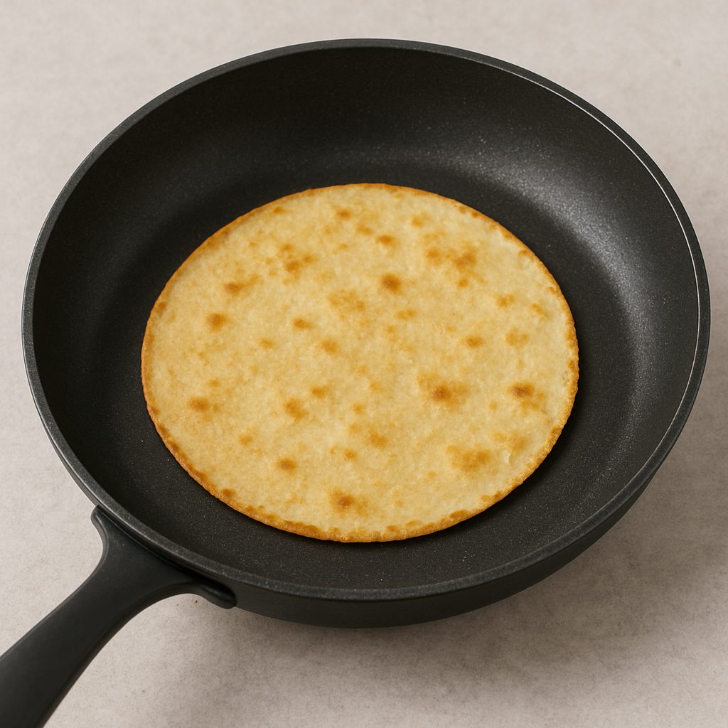 Tortilla de maíz dorándose en una sartén caliente, lista para ser utilizada en el montaje de tacos.